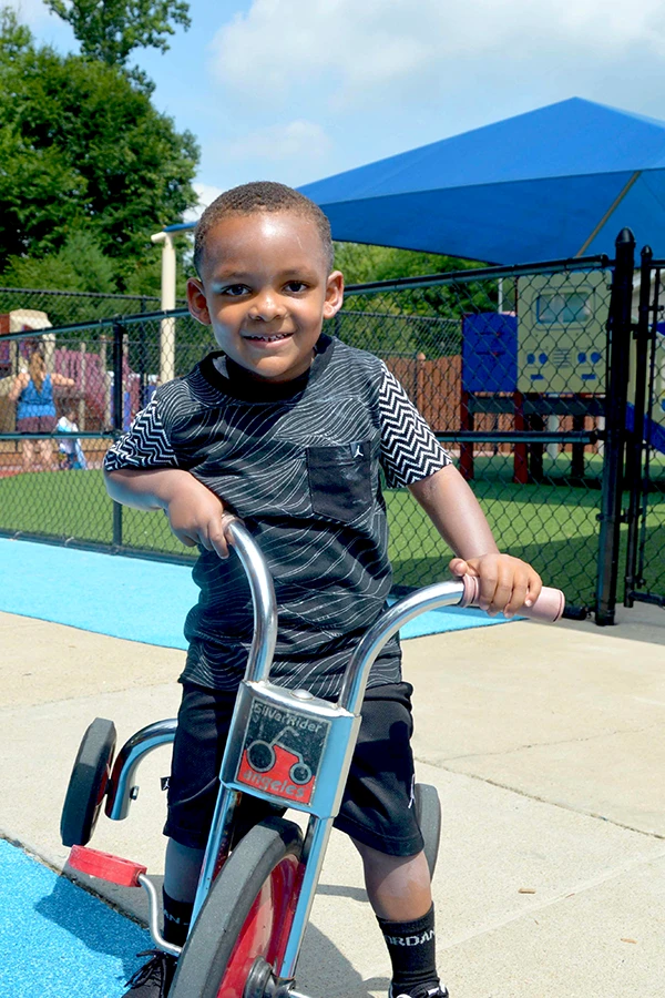 Enrollment at Learning Paths Academy - smiling young boy riding tricycle on playground