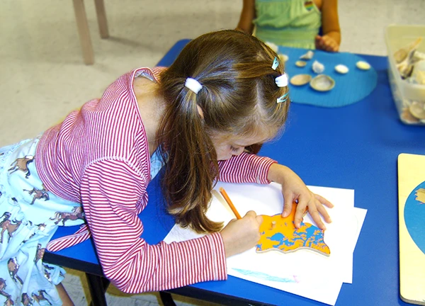 Montessori program - young girl tracing map block on paper